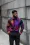 Man in vibrant, colorfully printed shirt and solid black pants, standing neutrally in a casual yet stylish outfit.